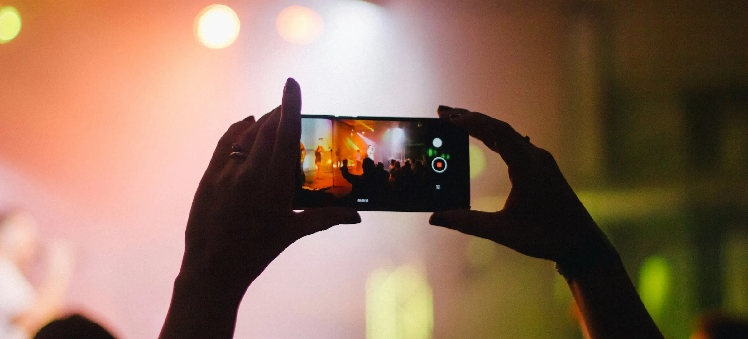 Two hands holding up a phone to film a concert stage